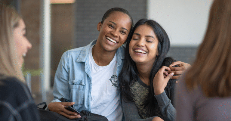 Two people smiling and leaning together, symbolizing how a leader’s emotional energy spreads and shapes the atmosphere of a team.