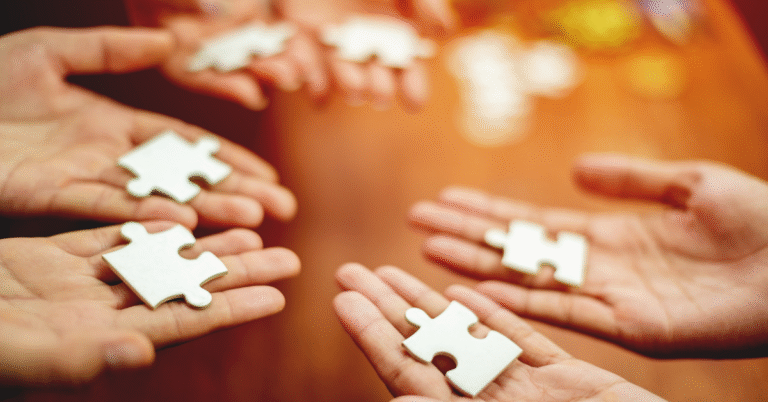Multiple hands holding puzzle pieces, symbolizing leadership bringing alignment in the first five minutes of a meeting so the team can fit their work together.